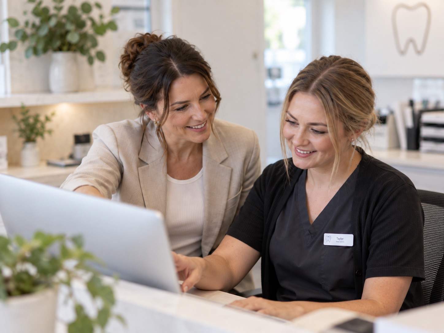 A consultant sitting beside a dental receptionist, pointing at something on a laptop